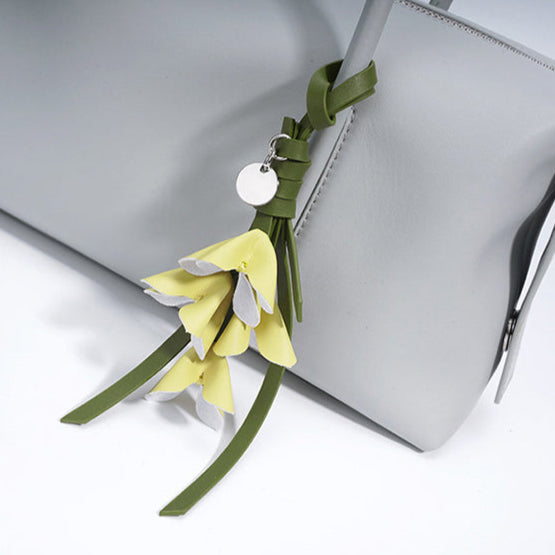 Hanging ornament with green ribbons and yellow flowers attached to a gray bag.